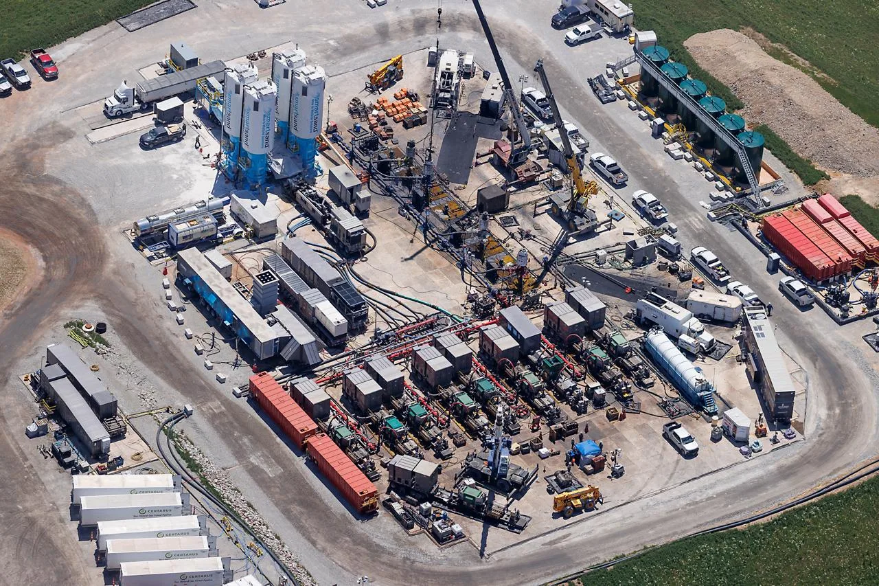 Aerial view of a busy frac spread and well-site pad — sand silos, pump units, and crew equipment mid-operation, the tempo Globeo books lodging against