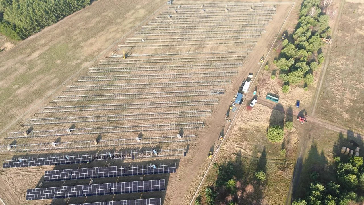 Aerial view of a large solar-farm construction site with rows of panel racking being installed across open land.