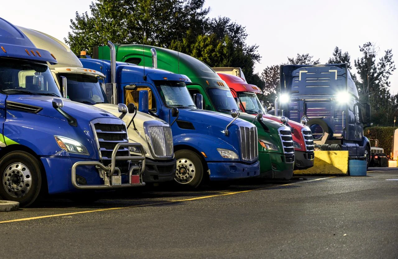 A row of colorful semi trucks parked side by side at a truck stop lot at dusk